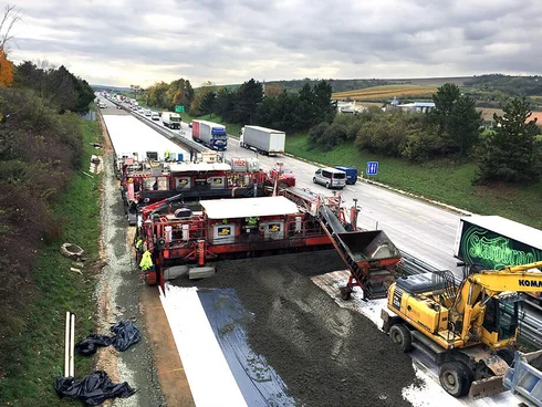 Foto: Zwei Betondeckenfertiger der OEBA beim Betonieren des linken Fahrbahnteils der tschechischen D2, dichter Verkehr auf dem dreispurigen rechten Fahrbahnteil