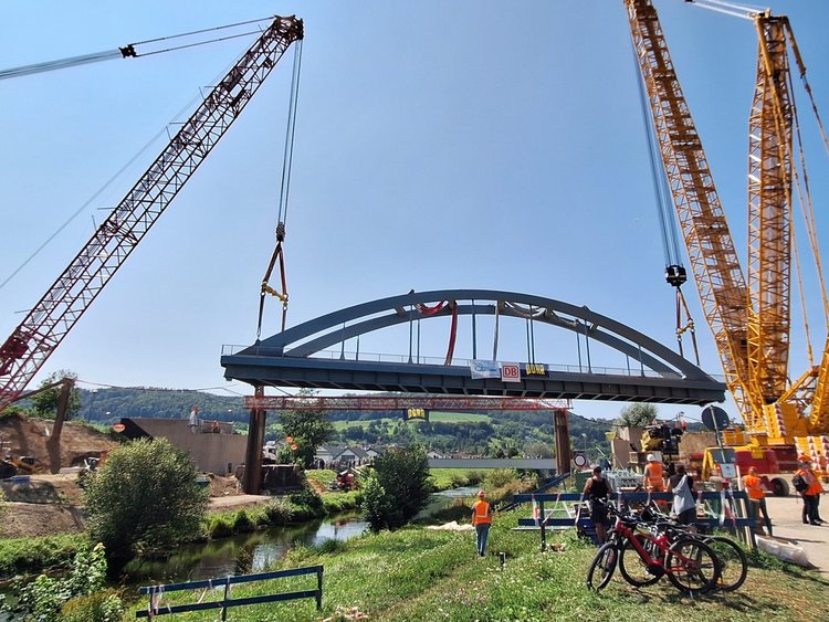 Heavyweight on the move. Two large cranes lift a steel bridge over a river.