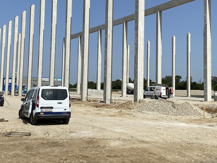 After the geothermal plant is before the hall construction. Building site with first pillars for the construction of a hall, on the right in the picture various building materials, next to it is a car, on the right in the picture other construction vehicles
